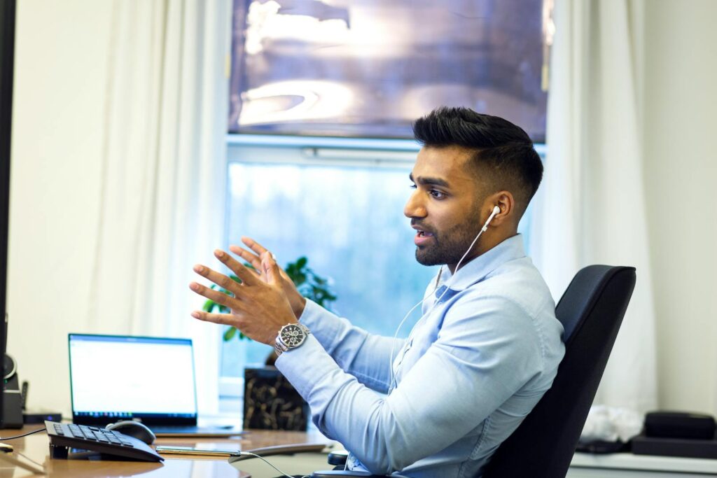 Adult male engaged in a virtual meeting using earphones in an office setting.