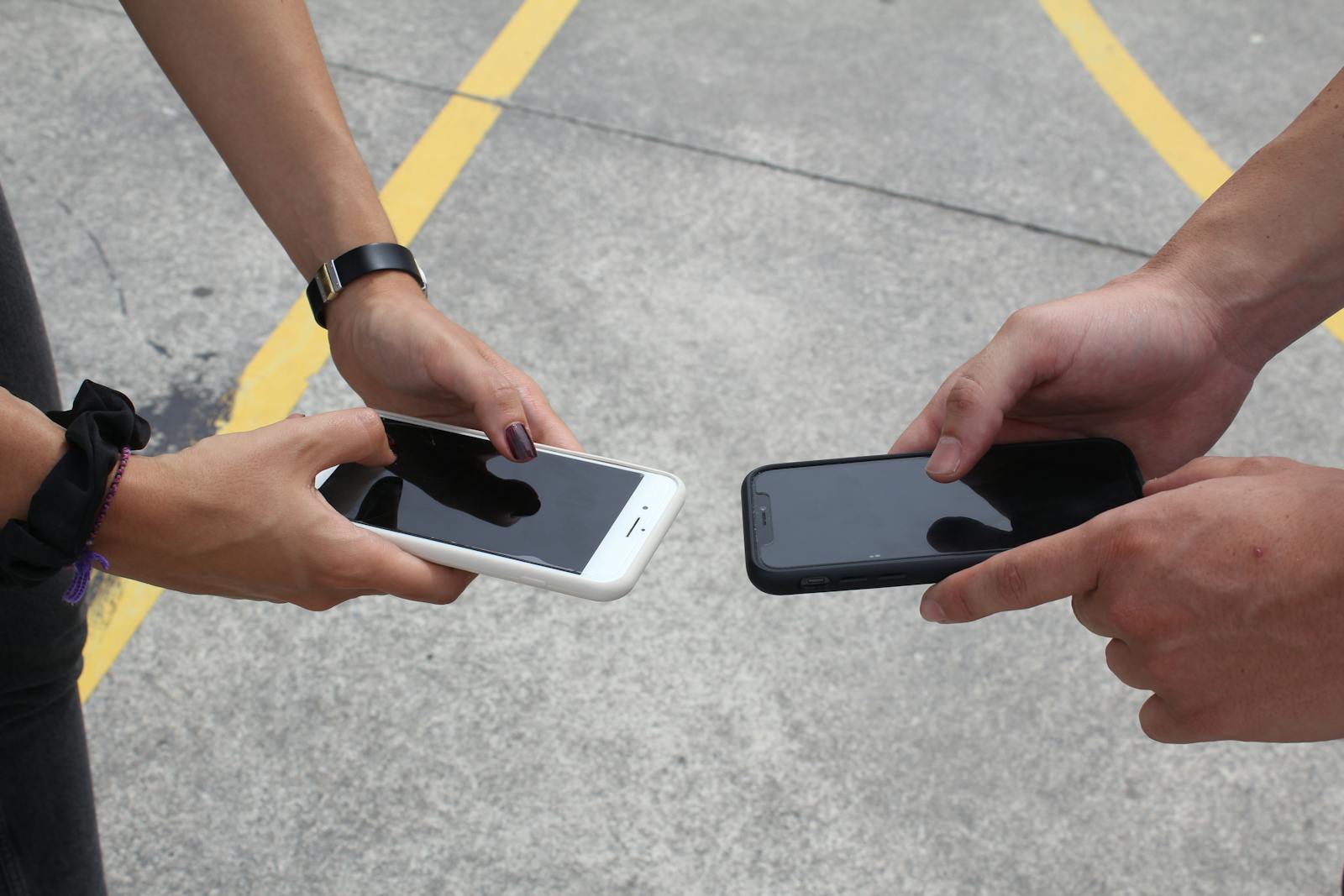 Two people exchanging or comparing smartphones in an outdoor setting, focusing on hands and technology.