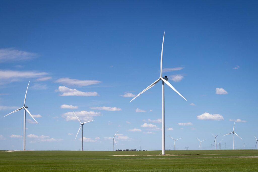 Wind turbines on green fields against a bright blue sky, highlighting renewable energy.