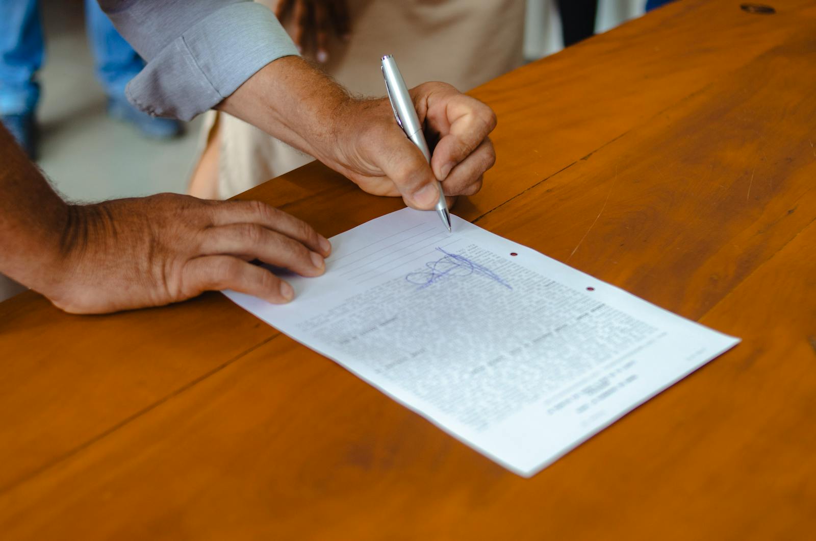 Close-up of a person signing a document on a wooden table, emphasizing detail and focus.