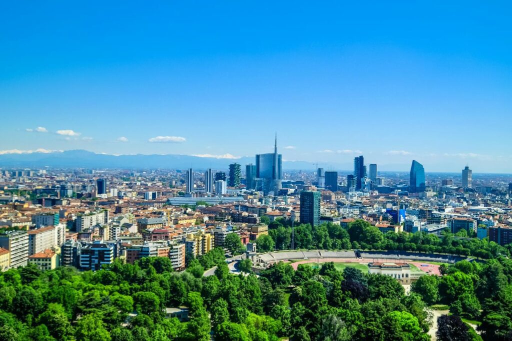 Panoramic view of Milan's skyline featuring modern skyscrapers and lush greenery under a clear blue sky.