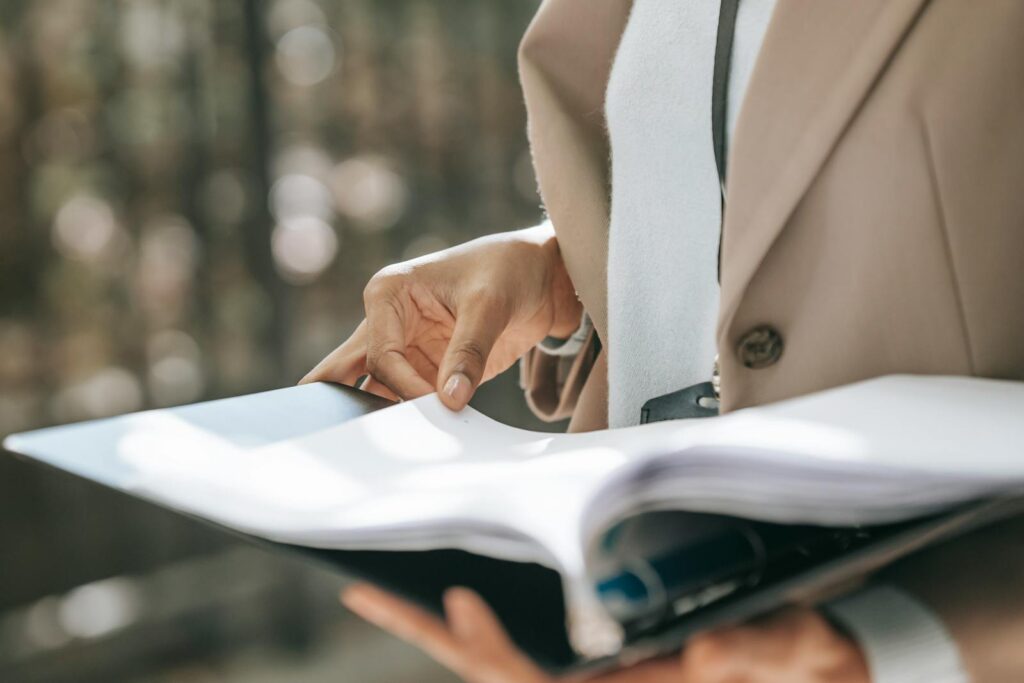 Crop faceless female entrepreneur in stylish jacket reading important documents in black folder